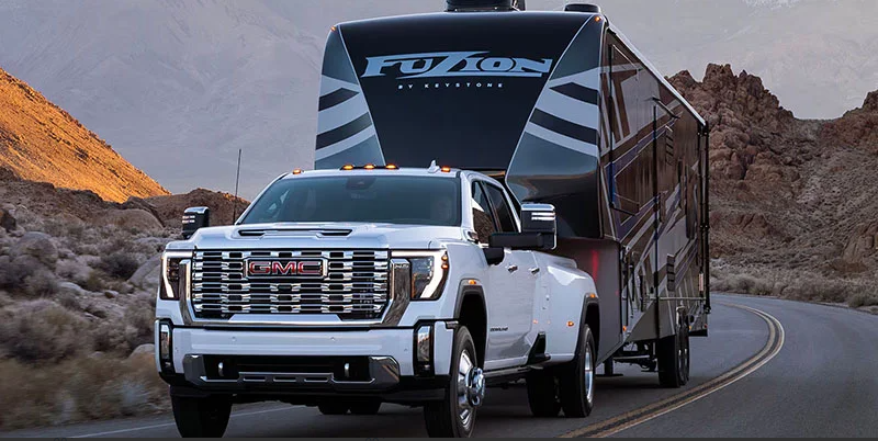 A 2025 GMC Sierra 2500 towing a camper down the road.